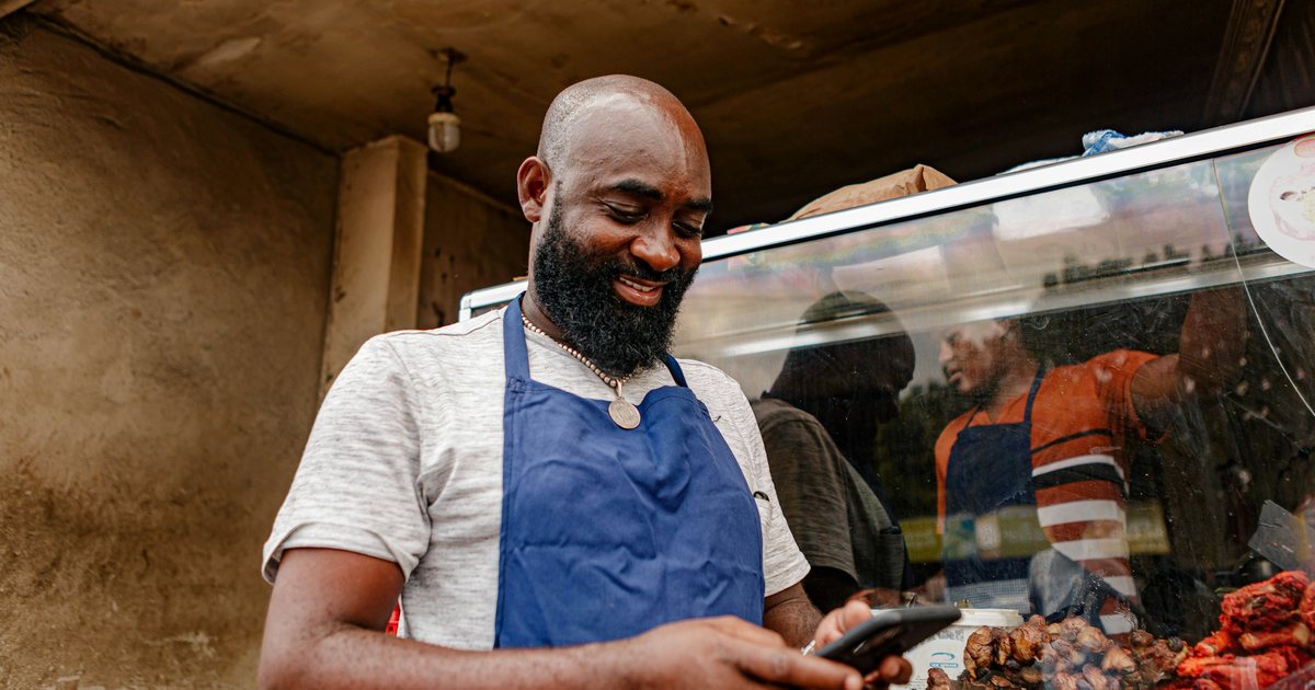 A shop owner in an apron checking his phone at the counter